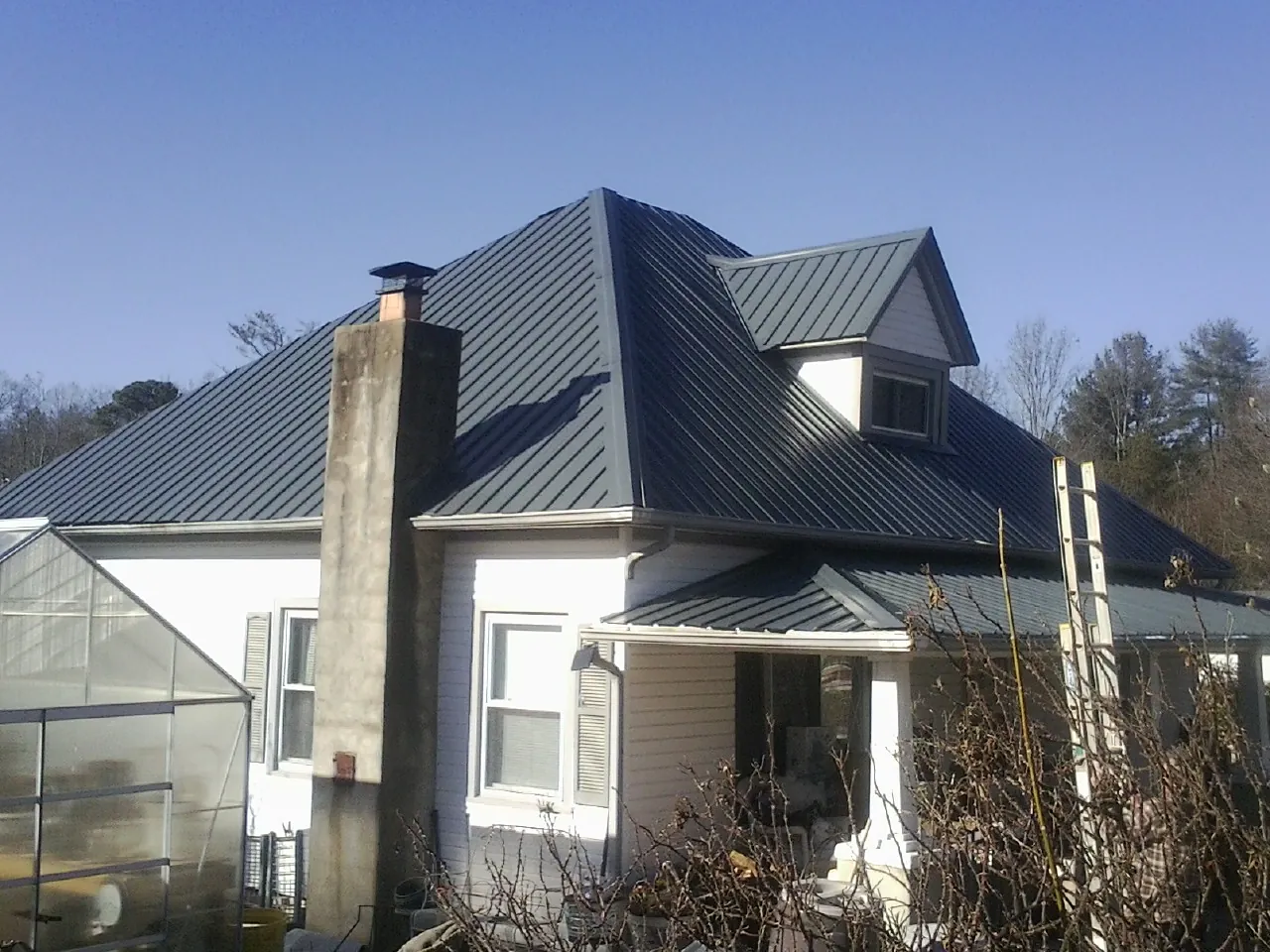 Dark blue standing seam metal roof on a white farmhouse with dormer — Slate & Tile Roof Repair by Roofing Brothers in Island