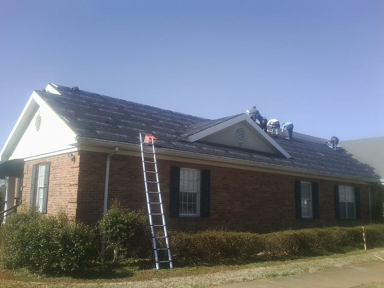 Crew tearing shingles off a brick ranch roof with a ladder set — Emergency Roof Repair work by our crew in Island
