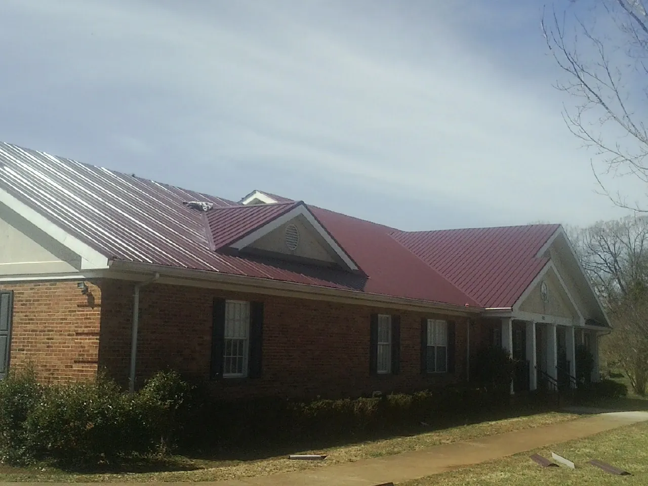 Red metal roof with gabled entries on a long brick building, from a Hail Damage Roof Repair job in Island