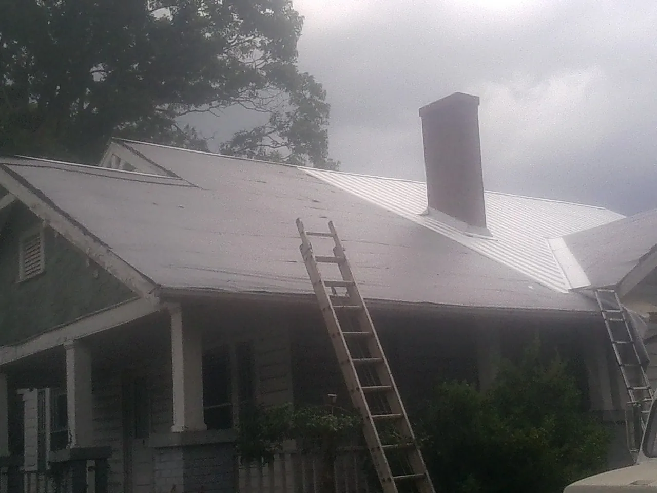 Ladders against a metal roof on an older home with a brick chimney in Island