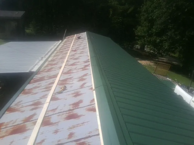 Old rusted panels beside newly installed green metal roofing — Wind Damage Roof Repair by Roofing Brothers in Island