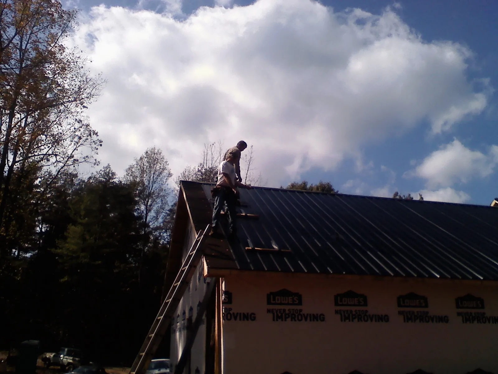 Roofer fastening dark metal panels high against a cloudy sky, from a Roof Inspection job in Island