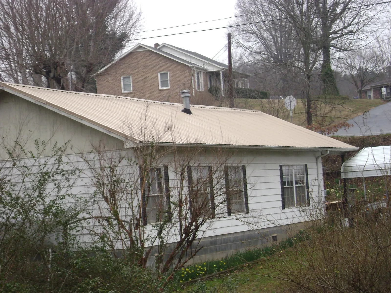 Tan metal roof on a white sided house set into a hillside — Commercial Roofing by Roofing Brothers in Island