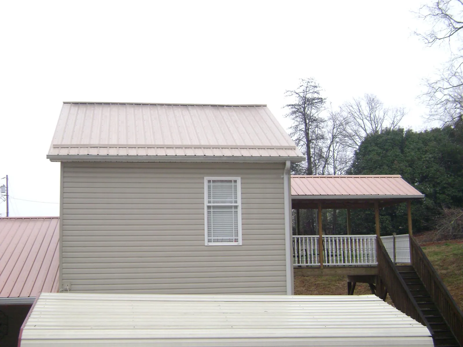 Tan metal roofs on a two story addition and attached porch, from a Roof Replacement job in Island